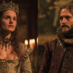 A crowned woman and a bearded man in elaborate Renaissance-style clothing facing forward in a candlelit hall