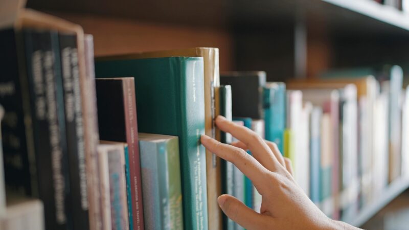 A hand reaches for a book on a crowded library shelf