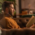 A man reads a book on a sofa in a warm, quiet room