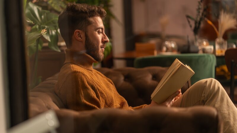 A man reads a book on a sofa in a warm, quiet room