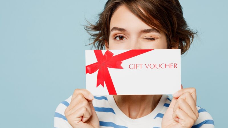 A woman holds a gift voucher in front of her face and winks